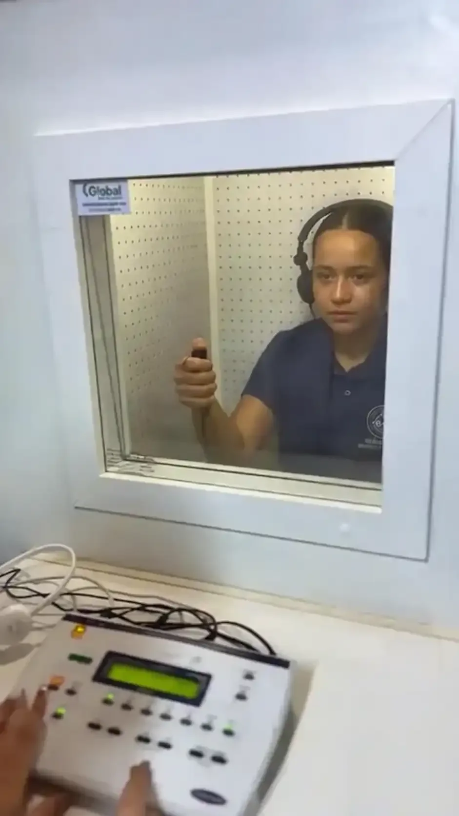 Paciente com fones em cabine de audiometria durante avaliação auditiva